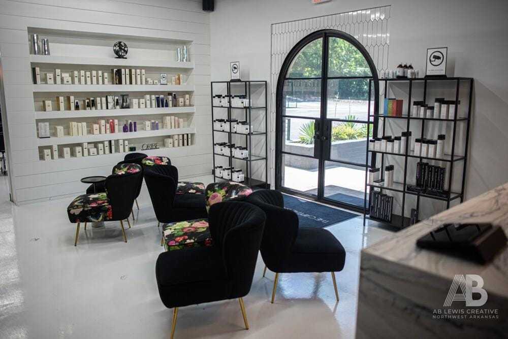 A modern salon lobby with black chairs, floral cushions, and shelves of beauty products.