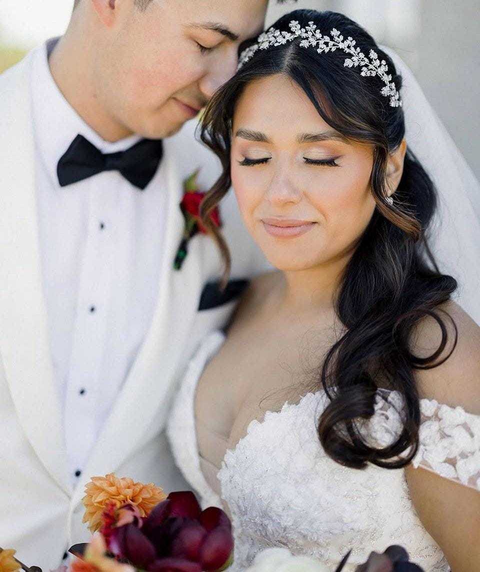 Bride and groom in wedding attire embracing, holding a bouquet of colorful flowers.