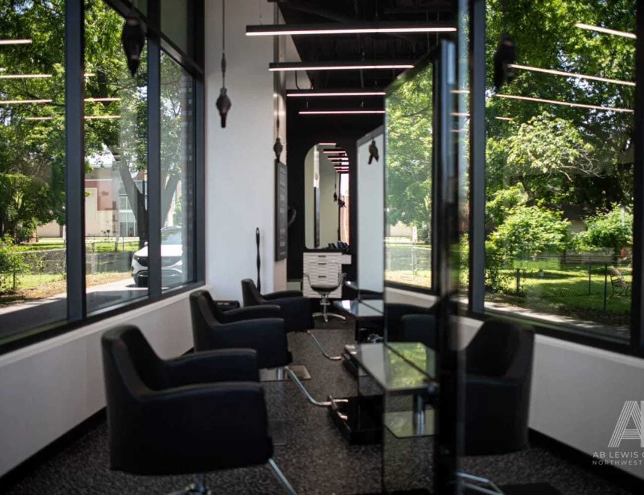 Modern barbershop interior with sleek black chairs and large windows facing a green landscape.